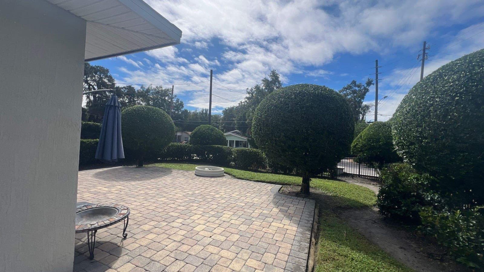 Wide paver patio with topiary boxwoods and umbrella in Central Florida — Firsthand Lawn and Landscape
